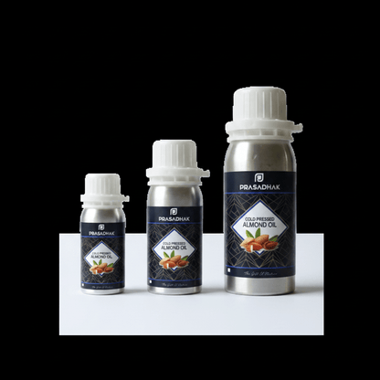 Three bottles of Prasadhak Gold-Premium Almond Oil in silver aluminum packaging with white caps, arranged by size on a white platform against a solid black background.