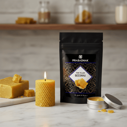 A black stand-up pouch of Prasadhak Dark Yellow Beeswax is displayed on a marble surface next to a yellow honeycomb candle, a bar of yellow wax, and an open tin of beeswax with its lid beside it.