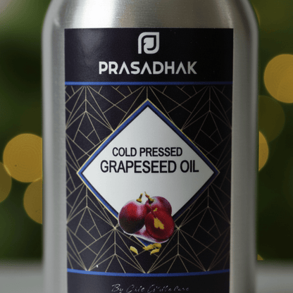 A close-up of a Prasadhak cold pressed grapeseed oil bottle, showing the label with grapefruit illustrations against a blurred green and gold bokeh background.