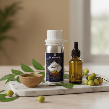 A bottle of Prasadhak Cold Pressed Neem Oil and a small amber dropper bottle are displayed on a marble tray with neem leaves and green neem fruits, set against a softly blurred indoor background.