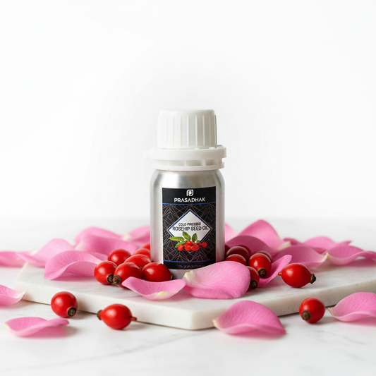 A small bottle of Prasadhak Rosehip Oil stands on a white marble slab surrounded by pink rose petals and red berries, against a clean white background.